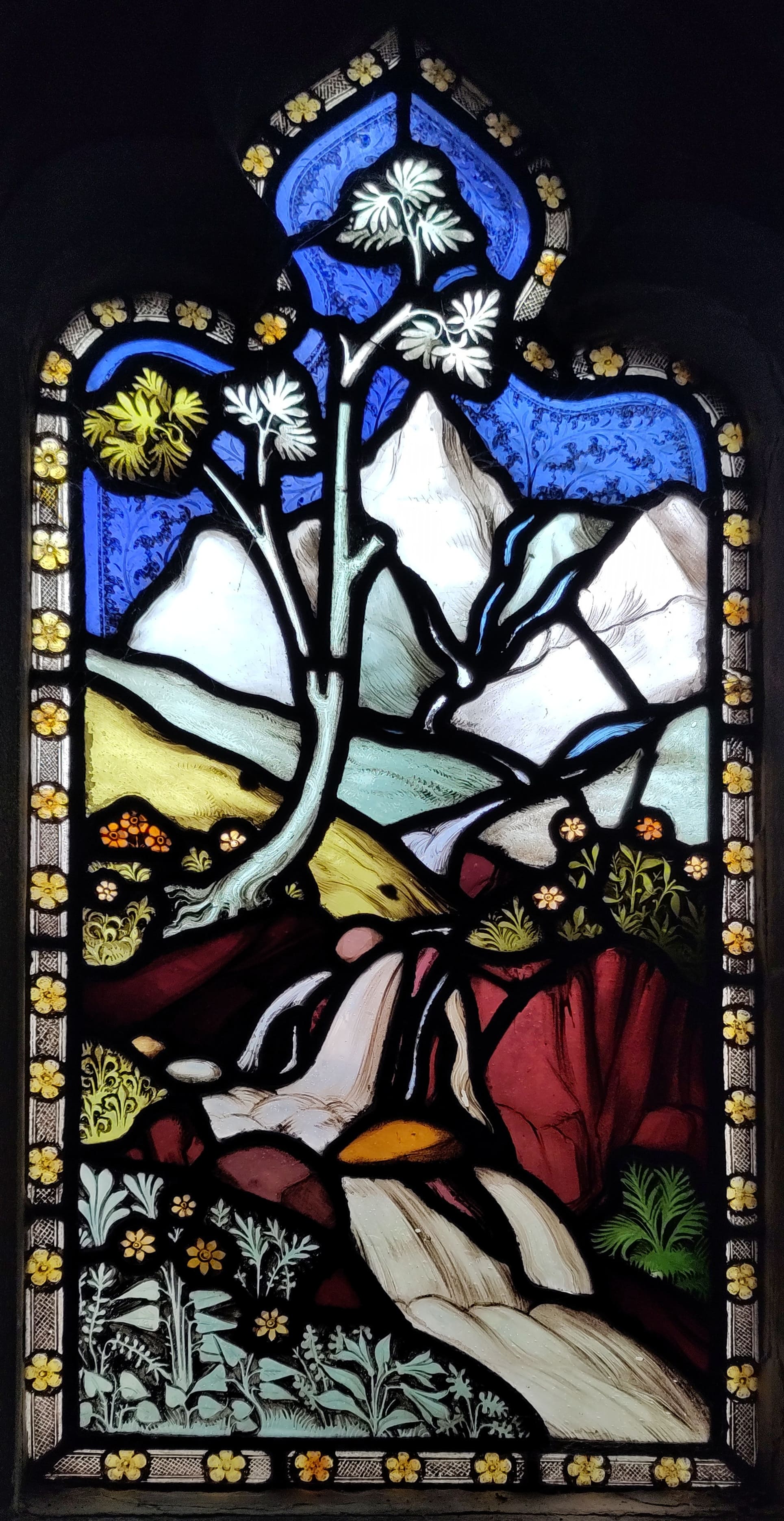 An image of a stained glass window. It depcits a landscape with mountains, trees and a waterfall flowing through the centre of the piece